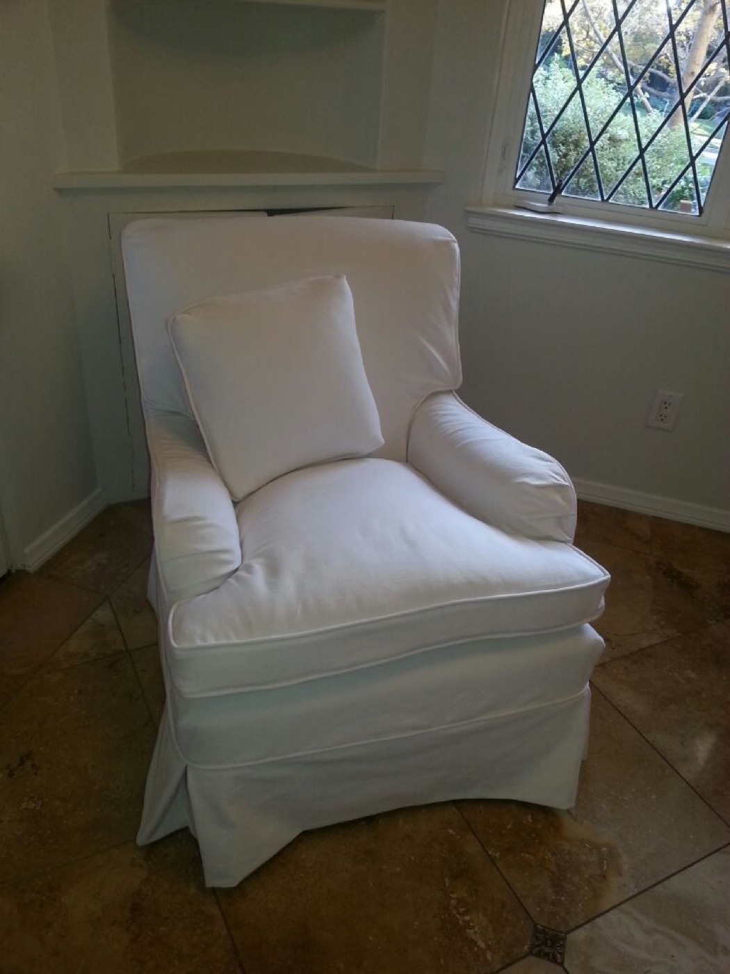 An armchair in a fitted white slipcover, beside a window.
