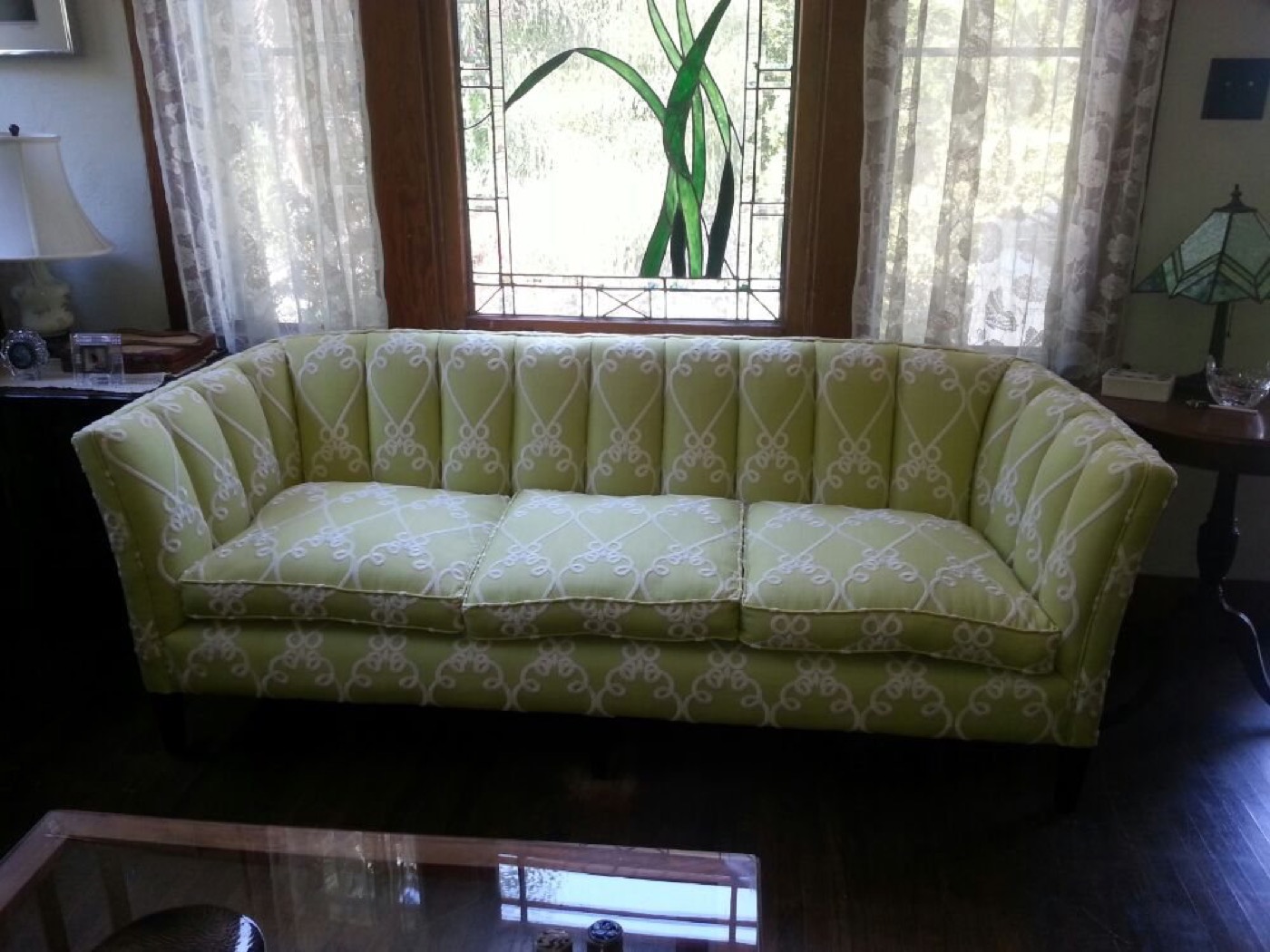 A long tufted sofa in soft green, under a bay window.