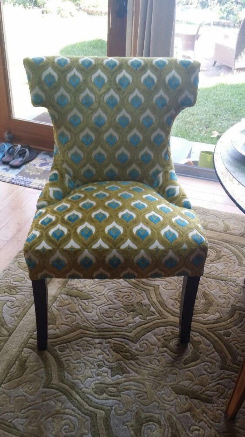 A dining chair in a teal and gold peacock-feather pattern.