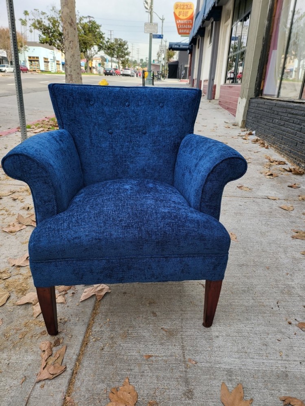 A deep blue velvet armchair we reupholstered, standing on the sidewalk outside our shop on Colorado Blvd.